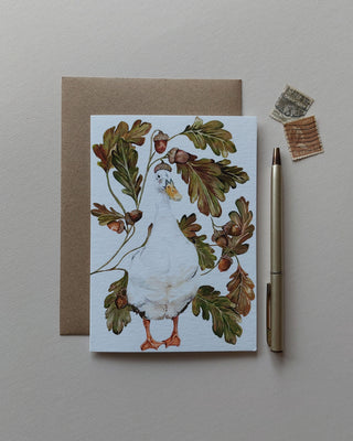 Indian runner duck wearing the hat of an acorn surrounded by acorns and foliage. Blank Card. 
