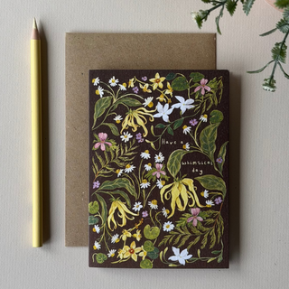 A botanical greeting card with a dark brown background and an illustrated floral pattern, placed on top of a kraft envelope. 