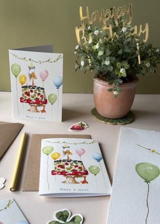 A styled flat-lay of birthday greeting cards featuring a watercolor illustration of a duck with birthday cake with balloons.