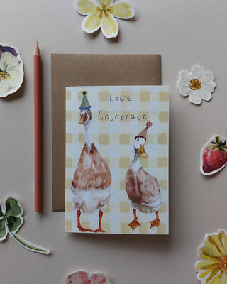 Greeting card illustrated with ducks wearing party hats on a gingham yellow background with text reading 'let's celebrate'