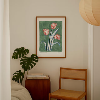 Muted turquoise painted background with electric blue and navy leaves and pink/peachy tulip flower heads. With small text reading  floral studies: tulip NO.3 styled in a dark wooden frame in a bedroom