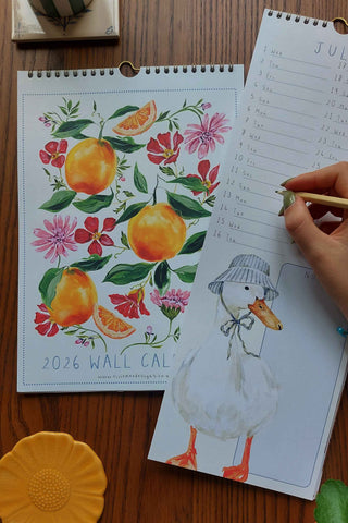 2026 wall calendar with floral and fruit design on a wooden surface.