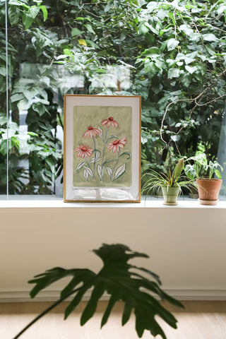 Our coneflower art print with a sage green painted background and peachy pink flowers and green outlined leaves. With small text reading ;floral studies: coneflower NO.7 styled against plants and greenery