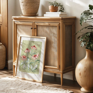 Our coneflower art print with a sage green painted background and peachy pink flowers and green outlined leaves. With small text reading floral studies: coneflower NO.7styled in a light oak frame against rattan furniture