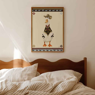 A framed wall art print featuring a cartoon duck dressed in western clothing, hanging above a wooden bed with striped bedding in a softly lit bedroom.