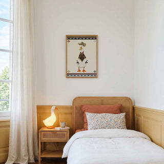 A styled bedroom interior featuring a single wooden bed with white bedding, a matching wooden nightstand with a lit lamp, and a framed decorative print on the wall. The room has warm wood paneling, a light rug, parquet flooring, and a large window with sheer curtains.