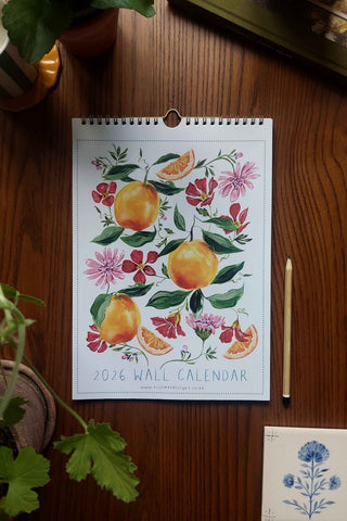 2026 wall calendar with floral and fruit design on a wooden surface