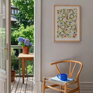 Garden Strawberries Print in light wood frame, styled A2 Print against white wall in kitchen with chair, and flower pots outside.