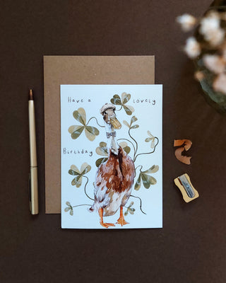 Greeting card with a duck illustration and 'Have a lovely Birthday' text, placed on a brown surface .