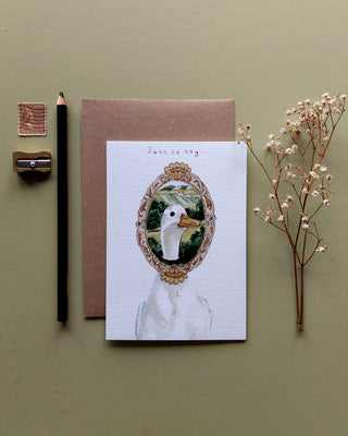 Greeting card with duck illustration on a green background with stationery items.
