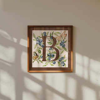 Framed artwork with letter 'B' surrounded by flowers and butterflies on a beige wall.