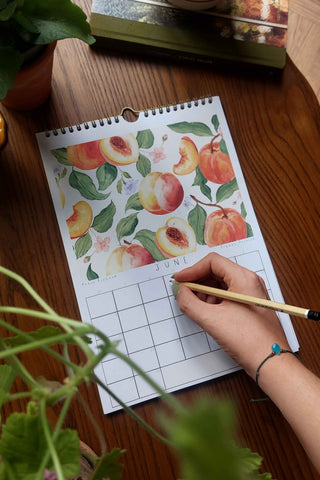 Person writing in a calendar with peach-themed design on a wooden desk