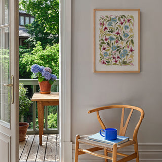 fuchsia print styled on blank wall by a chair, door open to show garden view with wooden table and plant pots on.