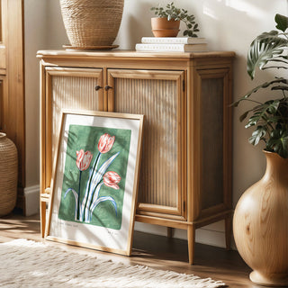 Muted turquoise painted background with electric blue and navy leaves and pink/peachy tulip flower heads. With small text reading floral studies: tulip NO.3 styled in light oak frame against rattan wood furniture