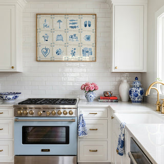 A light blue vintage-style gas range stove with gold knobs, set in a bright white kitchen with a subway tile backsplash and blue-and-white ceramic accents.