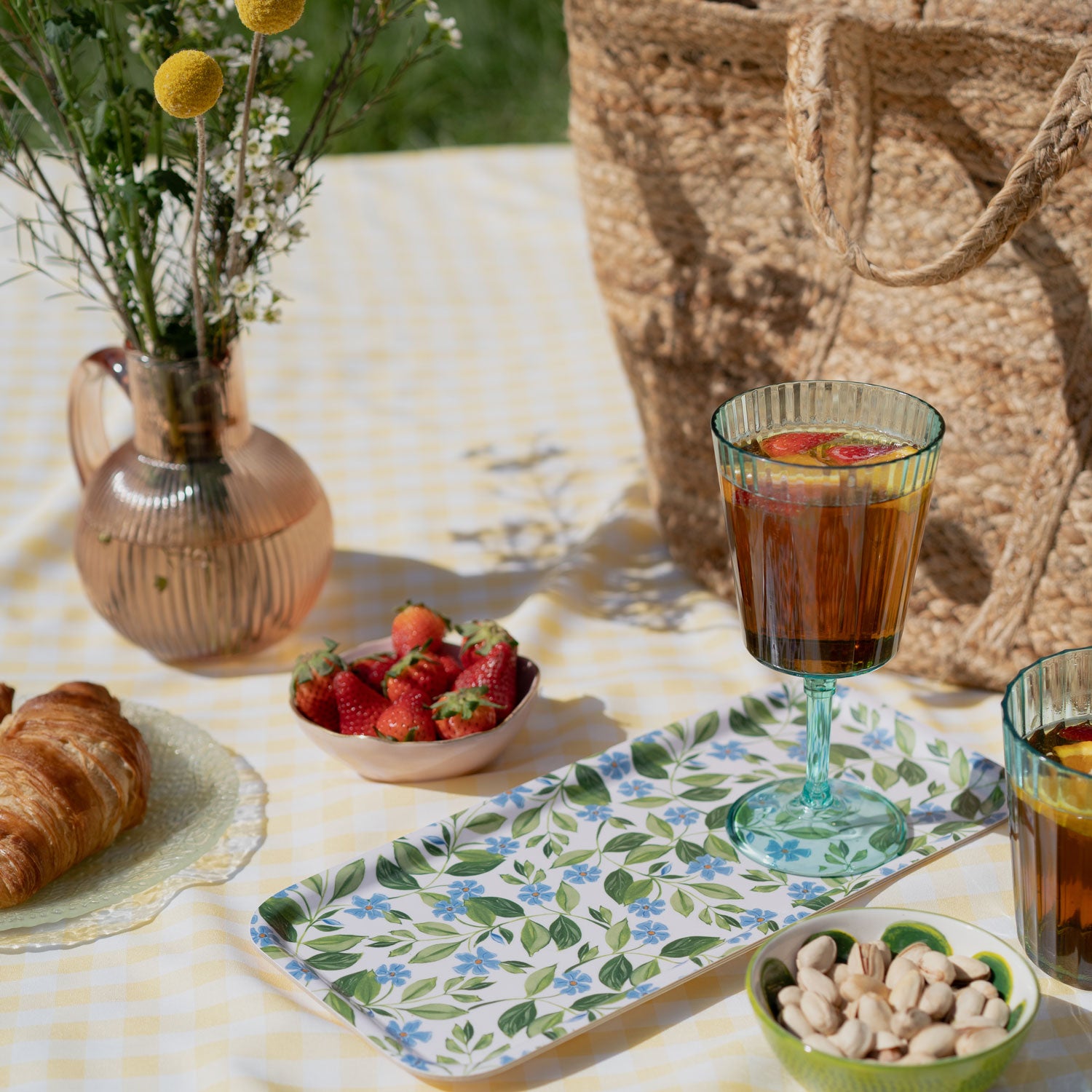 tray on yellow gingham rug, holding a glass of summer fruit drink.